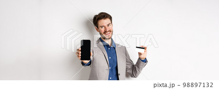 Online shopping. Successful businessman holding plastic credit card and showing mobile screen, smiling satisfied, making money, white background 98897132