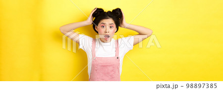 Shocked asian girl gasping worried, checking her hairstyle, standing anxious on yellow background 98897385