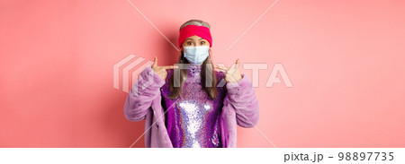Covid-19, social distancing and fashion concept. Asian edlerly woman in stylish party outfit and respirator, pointing fingers at face mask, asking to follow coronavirus quarantine rules 98897735