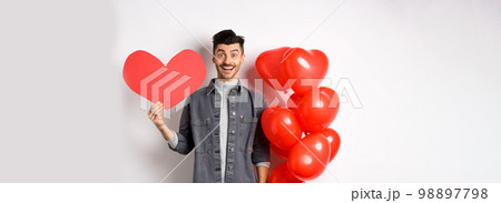 Valentines day and love concept. Cheerful funny guy showing heart cutout, standing near romantic balloons and smiling excited at camera, white background 98897798