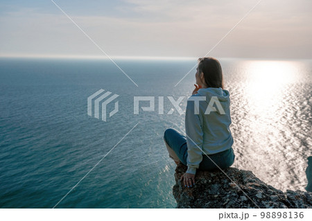 A young tourist Woman enjoying sunset over sea mountain landscape while sitting outdoor. Women's yoga fitness routine. Healthy lifestyle, harmony and meditation 98898136