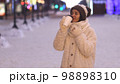 Winter portrait of a young woman in warm clothing warming herself with a hot drink. 98898310
