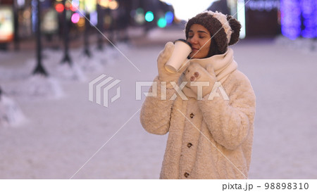 Winter portrait of a young woman in warm clothing warming herself with a hot drink. 98898310
