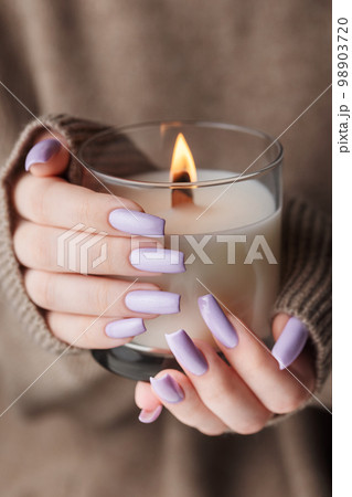 The hands of a young girl with a beautiful light purple manicure hold a candle The hands of a young girl with a beautiful light purple manicure hold a candle 98903720