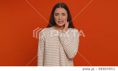 Woman touching cheek suffering from toothache cavities or gingivitis waiting for dentist appointment Woman touching cheek suffering from toothache cavities or gingivitis waiting for dentist appointment 98904951