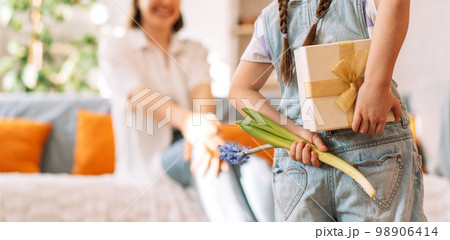 A child holding a gift and flowers behind her back in front of her mother, mother's day A child holding a gift and flowers behind her back in front of her mother, mother's day 98906414