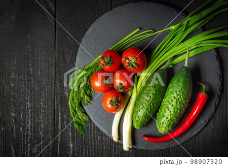 Vitamin set for fresh vegetable salad. Red tomatoes and green young onions with cucumber on a plate Vitamin set for fresh vegetable salad. Red tomatoes and green young onions with cucumber on a plate 98907320
