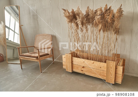 Dried flowers in a wooden box on the floor next to the chair. Sunlight and sun rays fall from the window. Minimalism in the interior. Space for copying. High quality photo 98908108