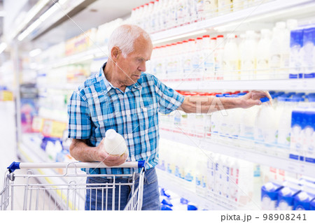 elderly retired man buying milk in dairy section of the supermarket elderly retired man buying milk in dairy section of the supermarket 98908241