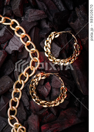 Golden chains earrings on black coals background. 98910670