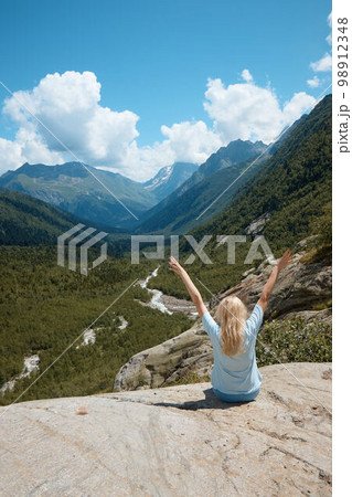 a girl sits on the edge of a cliff and looks into the distance, in the distance there is a river and a gorge, a good mood, clouds and a mountain landscape a girl sits on the edge of a cliff and looks into the distance, in the distance there is a river and a gorge, a good mood, clouds and a mountain landscape 98912348