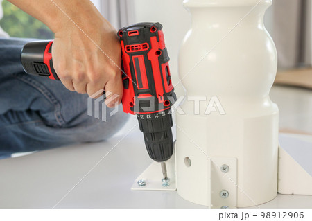 man assembling white table furniture at home using cordless screwdriver 98912906