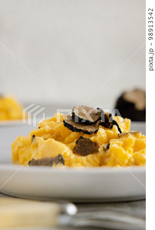 Scrambled eggs with fresh black truffles from Italy served in a plate close up, gourmet breakfast 98913542