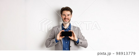 E-commerce and online shopping concept. Happy guy in business suit showing empty smartphone screen horizontally, smiling pleased at camera, white background E-commerce and online shopping concept. Happy guy in business suit showing empty smartphone screen horizontally, smiling pleased at camera, white background 98913779