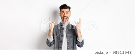 Excited funny guy showing tongue and heavy metal horns sign, enjoying party or event, having fun, standing on white background Excited funny guy showing tongue and heavy metal horns sign, enjoying party or event, having fun, standing on white background 98913948
