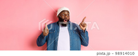 Happy african-american man showing thumb-up and pointing at upper left corner copy space, praising good deal, standing over pink background 98914010
