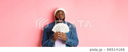 Amazed african-american man receive cash prize, showing money and staring at camera in awe, standing over pink background Amazed african-american man receive cash prize, showing money and staring at camera in awe, standing over pink background 98914166