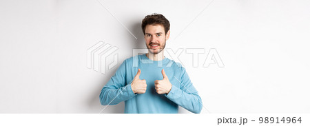 Good choice. Attractive caucasian man with beard showing thumbs up and smiling, like and approve good product, recommending something, standing on white background 98914964