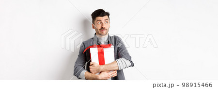 Excited man hugging romantic gift for girlfriend, waiting for valentines date with lover, looking at empty space logo with happy face, standing on white background Excited man hugging romantic gift for girlfriend, waiting for valentines date with lover, looking at empty space logo with happy face, standing on white background 98915466