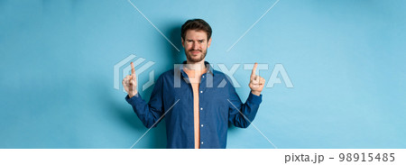 Skeptical young man frowning and squinting, cringe from something disgusting, standing on blue background Skeptical young man frowning and squinting, cringe from something disgusting, standing on blue background 98915485