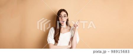 Creative young woman in glasses pitching idea, raising finger in eureka sign and gasping, have a plan, standing on beige background 98915683