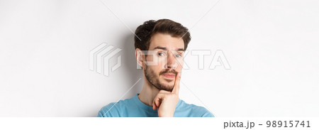 Image of thoughtful young man with beard, making choice, touching lip and looking pensive at camera, deciding something, white background Image of thoughtful young man with beard, making choice, touching lip and looking pensive at camera, deciding something, white background 98915741