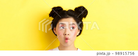 Close-up of teen asian girl pucker lips and looking funny at camera, standing with glamour makeup and stylish hairstyle, yellow background Close-up of teen asian girl pucker lips and looking funny at camera, standing with glamour makeup and stylish hairstyle, yellow background 98915756