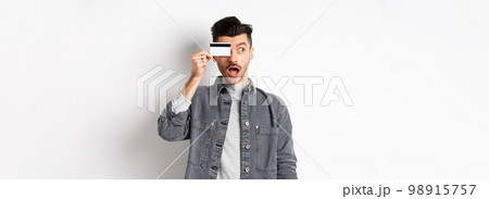 Excited funny guy look aside at logo and show plastic credit card, standing amazed on white background 98915757