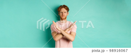 Skeptical redhead man in t-shirt saying no, cross arms on chest and frowning disappointed, prohibit something bad, standing over turquoise background Skeptical redhead man in t-shirt saying no, cross arms on chest and frowning disappointed, prohibit something bad, standing over turquoise background 98916067