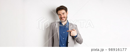Modest smiling man in suit pointing at himself with cute face, self-promoting, standing on white background 98916177