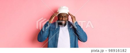 Distressed Black man having headache, touching head and grimacing with concerned face, standing over pink background Distressed Black man having headache, touching head and grimacing with concerned face, standing over pink background 98916182