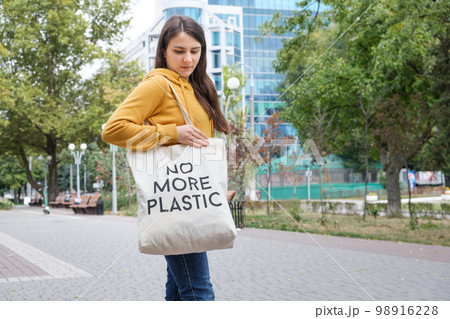 A woman shows a fabric reusable bag with the text no more plastic. 98916228