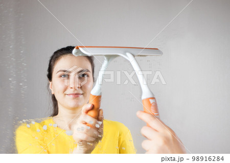 The cleaning lady cleans the mirror with a water dispenser and window cleaner. House cleaning. Cleaning service. 98916284