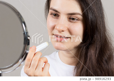 A woman paints her lips with a therapeutic balm. Treatment of cracks and dry lips, weathered lips A woman paints her lips with a therapeutic balm. Treatment of cracks and dry lips, weathered lips 98916293