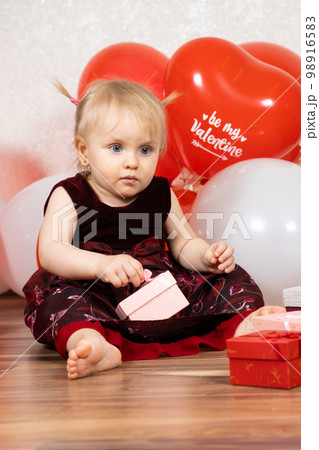 Cute little girl opens gifts sitting among the balls. Children and Valentine's Day. Cute little girl opens gifts sitting among the balls. Children and Valentine's Day. 98916583