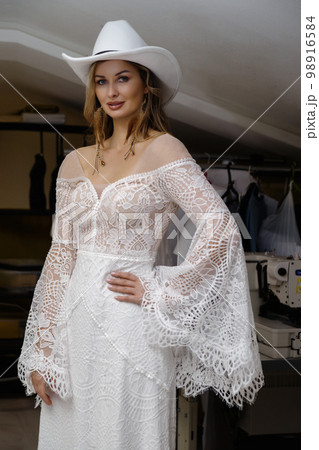 A girl in a boho wedding dress in a sewing workshop. 98916584