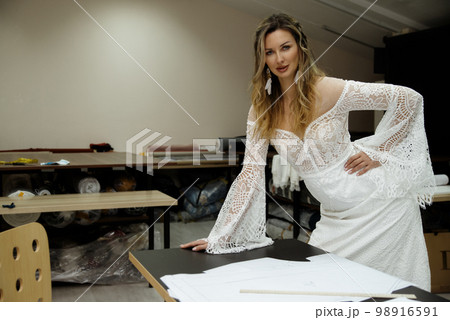 A girl in a boho wedding dress in a sewing workshop. 98916591