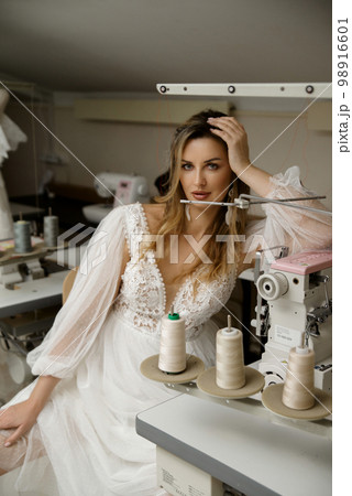 A girl in a boho wedding dress in a sewing workshop. A girl in a boho wedding dress in a sewing workshop. 98916601