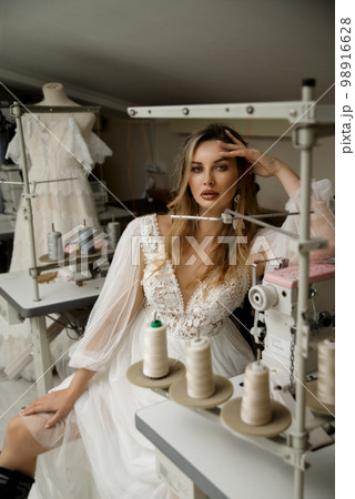 A girl in a boho wedding dress in a sewing workshop. A girl in a boho wedding dress in a sewing workshop. 98916628