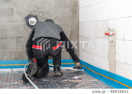 a worker installs underfloor heating in a new building 98916641