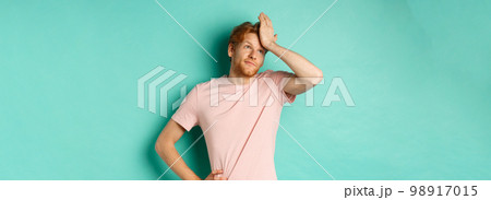 Annoyed and bothered redhead male model showing facepalm and roll eyes, standing over mint background 98917015