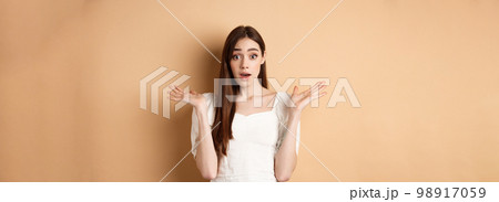 Surprised caucasian girl look with disbelief and amazement, spread hands sideways and gasping confused, cant understand what happening, know nothing, standing on beige background 98917059