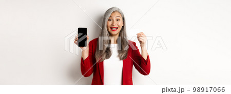 Cheerful asian mature woman showing blank smartphone screen and credit card, concept of e-commerce Cheerful asian mature woman showing blank smartphone screen and credit card, concept of e-commerce 98917066