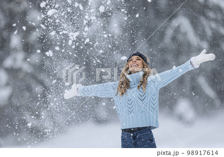 With arms wide open, woman in blue sweater, white gloves, scarf and hat enjoys fresh air on a snowy winter day 98917614