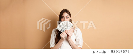 Excited girl showing dollar bills and raising eyebrows amazed, making money, standing on beige background 98917672