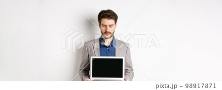 Handsome caucasian businessman in suit showing empty laptop screen, demonstrate promo, standing on white background Handsome caucasian businessman in suit showing empty laptop screen, demonstrate promo, standing on white background 98917871