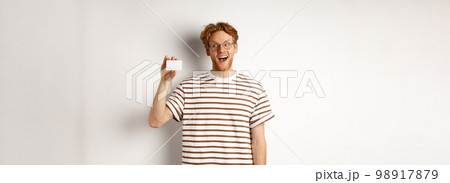Shopping and finance concept. Amazed caucasian redhead man showing plastic card, saying wow and staring impressed at camera, white background Shopping and finance concept. Amazed caucasian redhead man showing plastic card, saying wow and staring impressed at camera, white background 98917879