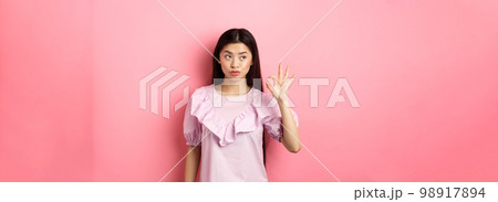 Sassy asian woman in dress show okay sign, looking aside, assure everything good, guarantee all OK, standing pleased on pink background Sassy asian woman in dress show okay sign, looking aside, assure everything good, guarantee all OK, standing pleased on pink background 98917894