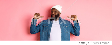 Confident and cheeky Black man pointing at himself, staring at camera self-assured, show-off, standing over pink background 98917962