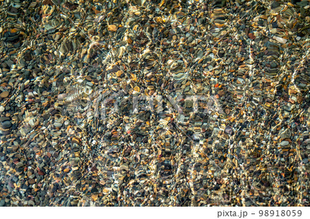 The texture of the bottom. Many small stones are visible under the clear water. Water ripples of the sea, sun rays on the rocks. The texture of the bottom. Many small stones are visible under the clear water. Water ripples of the sea, sun rays on the rocks. 98918059